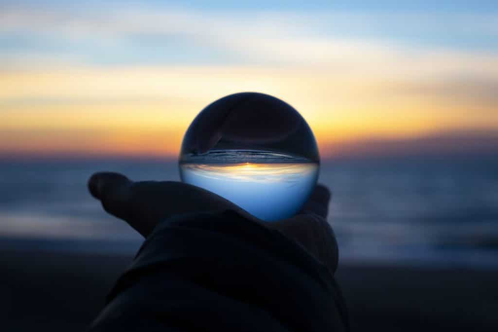 pessoa segurando uma bola de contato, que está refletindo o nascer do sol do horizonte