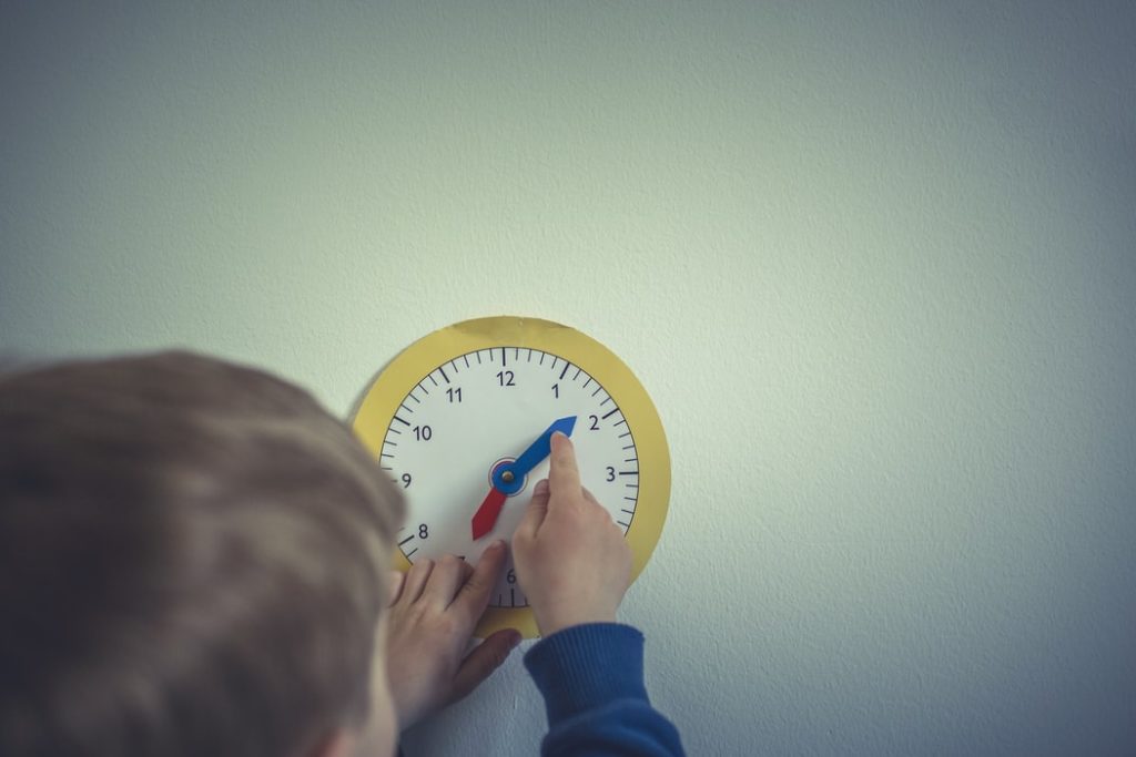 criança ajustando ponteiro de um relógio de papel apoiado na parede
