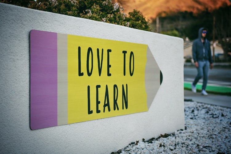 parece com placa em formato de lápis onde está escrito "love to learn"